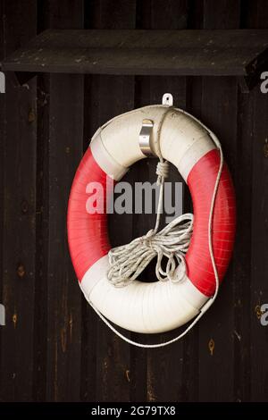 Lifebuoy con corda galleggiante appesa su pareti di legno scuro Foto Stock