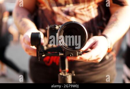 Un uomo con una macchina fotografica e un obiettivo. Fotocamera sullo stabilizzatore per riprese video. Sfondo sfocato e riflesso del sole Foto Stock