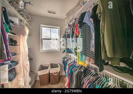 Una piccola e piena passeggiata nell'armadio con finestra e cestini di lavanderia Foto Stock