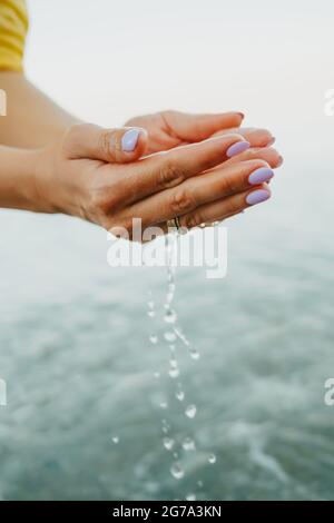 L'acqua che versa dalle mani del donna. Mare, vicino alle braccia femminili. Camicia gialla sullo sfondo. L'acqua è una forza vitale Foto Stock