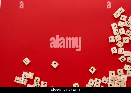 Immagine di sfondo le lettere sono sparse in disordine. Lettere inglesi. Lettere quadrate di legno su sfondo rosso brillante. Biglietto d'auguri, pronto all'uso Foto Stock