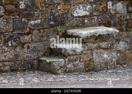 Vecchio blocco di montaggio per equitazione stagionato su un muro in un cortile di campagna inglese Foto Stock