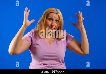 Media età bella donna bionda che indossa camicia viola casual in piedi su sfondo blu che soffre di mal di testa disperata e stressata perché pai Foto Stock