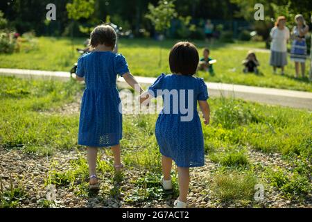 Preschoolers sulla strada. Le ragazze stanno camminando per strada. Vacanze con bambini in estate. I bambini in abiti identici stanno tenendo le mani Foto Stock