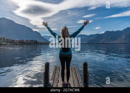 Donna non riconosciuta che indossa abiti sportivi sollevando le braccia e godendo la vista delle montagne. Foto Stock