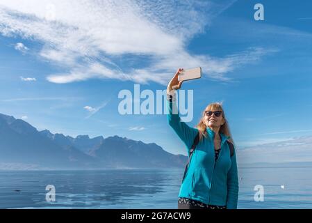 Donna felice godendo di giorno in montagna e prendendo un selfie con il suo telefono. Foto Stock