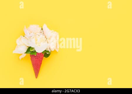 Fiori di pony bianchi in un cono gelato al cialde rosso su uno sfondo giallo brillante. Festa della mamma, San Valentino, bachelorette, concetto estivo. Foto Stock