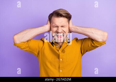 Ritratto di attraente ragazzo disperato che chiude le orecchie urlando isolato su sfondo viola di colore viola viola Foto Stock