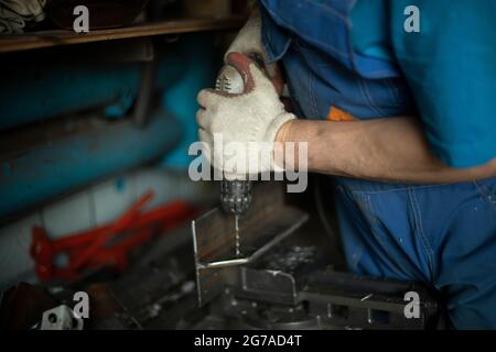 Forare il metallo con un trapano. L'uomo sta lavorando. Foratura in acciaio. Lavorare in un'officina di lavorazione del metallo. Foto Stock