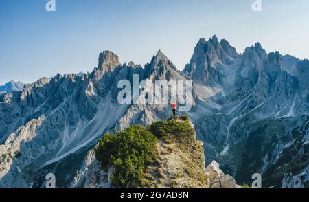 Vista aerea di un uomo con le mani alzate sul bordo superiore ammirando le cime epiche dei Cadini di Misurina, le Alpi Italiane, le Dolomiti, l'Italia, l'Europa Foto Stock