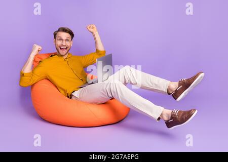 Profilo full size foto laterale del giovane uomo felice positivo sorriso gioire vittoria fortunato laptop isolato su sfondo di colore viola Foto Stock