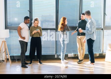 Vista frontale dei giovani colleghi multietnici che si divertono a conversare durante la pausa caffè in un ufficio moderno. Foto Stock