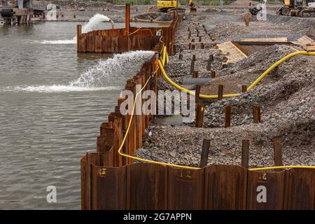 Goteborg, Svezia - maggio 16 2021: L'acqua viene pompata da dietro una barriera metallica che rivendica terreni per la costruzione Foto Stock