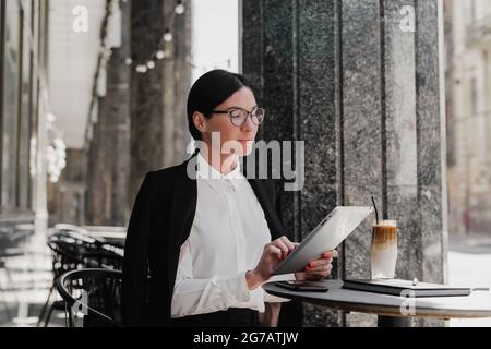 Elegante donna d'affari con computer tablet che beve caffè al bar. Foto Stock