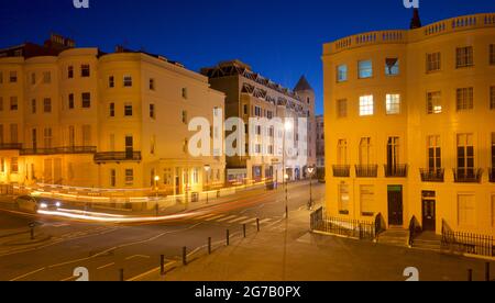 Incrocio della parte inferiore di Brunswick Place in cima a Brunswick Square e Western Road, Hove. Dawn. Alloggiamento Regency illuminato da lampioni. Trais leggero da veicolo stradale in transito. Brighton & Hove, East Sussex, Inghilterra, Regno Unito Foto Stock