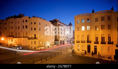 Incrocio della parte inferiore di Brunswick Place in cima a Brunswick Square e Western Road, Hove. Dawn. Alloggiamento Regency illuminato da lampioni. Trais leggero da veicolo stradale in transito. Brighton & Hove, East Sussex, Inghilterra, Regno Unito Foto Stock