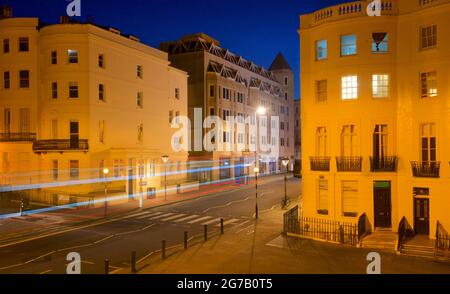 Incrocio della parte inferiore di Brunswick Place in cima a Brunswick Square e Western Road, Hove. Dawn. Alloggiamento Regency illuminato da lampioni. Trais leggero da veicolo stradale in transito. Brighton & Hove, East Sussex, Inghilterra, Regno Unito Foto Stock