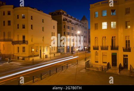 Incrocio della parte inferiore di Brunswick Place in cima a Brunswick Square e Western Road, Hove. Dawn. Alloggiamento Regency illuminato da lampioni. Trais leggero da veicolo stradale in transito. Brighton & Hove, East Sussex, Inghilterra, Regno Unito Foto Stock