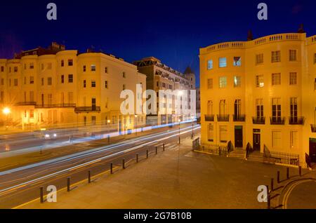 Incrocio della parte inferiore di Brunswick Place in cima a Brunswick Square e Western Road, Hove. Dawn. Alloggiamento Regency illuminato da lampioni. Trais leggero da veicolo stradale in transito. Brighton & Hove, East Sussex, Inghilterra, Regno Unito Foto Stock