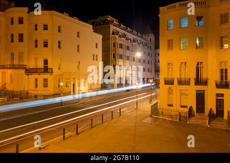 Incrocio della parte inferiore di Brunswick Place in cima a Brunswick Square e Western Road, Hove. Dawn. Alloggiamento Regency illuminato da lampioni. Trais leggero da veicolo stradale in transito. Brighton & Hove, East Sussex, Inghilterra, Regno Unito Foto Stock