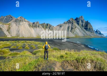 Uomo escursionista con zaino a dune di sabbia nera sul promontorio di Stokksnes sulla costa sud-orientale islandese con Vestrahorn. Colorata estate mattina Islanda, Europa. Foto Stock