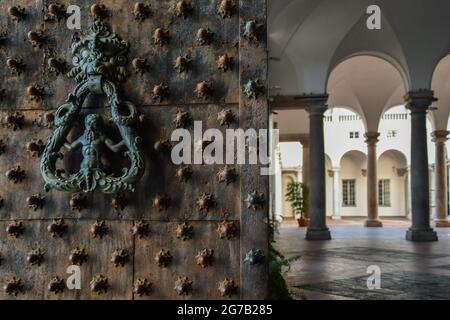 Porta chiodata di Palazzo Ducale con il tipico batticalcagno raffigurante un tritone e il portico colonnato sullo sfondo, Genova, Liguria, Italia Foto Stock