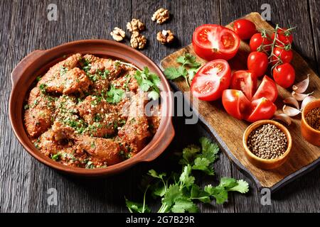 Chakhokhbili, pollo stufato, pomodoro con erbe fresche, noci e spezie in una pentola di argilla su un tavolo di legno con ingredienti su un tagliere, georgia Foto Stock