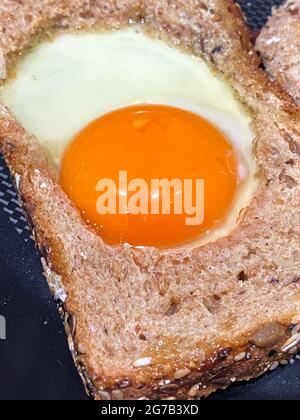 Uova all'interno di una fetta di pane tostato di grano per la colazione. In un cestino sono anche note come uova. Foto Stock