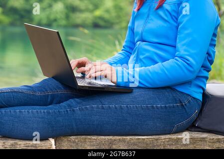 Giovane donna, donna freelance che lavora con un computer portatile con bella vista sulla foresta e sul lago. Foto Stock