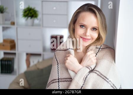 Foto di bella adorabile signora bionda godere di relax guardare fotocamera sorriso coperto plaid in camera confortevole al coperto Foto Stock