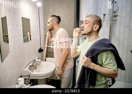 Giovani uomini spazzolando i denti di fronte agli specchi in bagno dormitorio al mattino Foto Stock