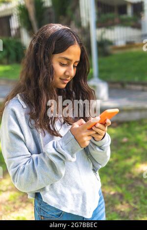 Latina bruna ragazza teen utilizzando il suo smartphone in una mattina all'aperto Foto Stock