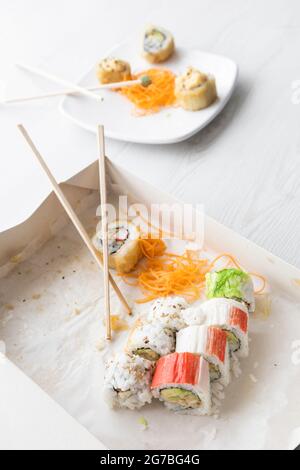 confezionamento in scatola di cartone, con pochi rotoli di sushi in fila e alcuni chopsticks, dietro un piatto con altri rotoli ordinati, dettagli della consistenza del cibo, Foto Stock