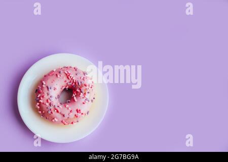Ciambella glassata di zucchero rosa su sfondo viola colorato. Foto Stock