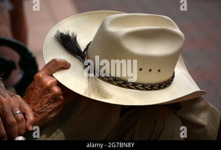 Un uomo che indossa stivali da cowboy e un cappello da cowboy Stetson di paglia si rilassa su una panchina del parco a Santa Fe, New Mexico. Foto Stock