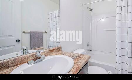 L'interno del bagno di Pano con la vasca da bagno e il lavandino bianco su un piano di marmo marrone Foto Stock