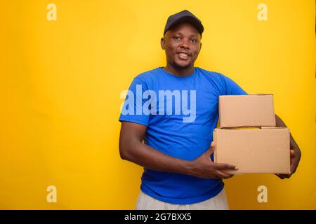 Un addetto alle consegne africano o un addetto alla spedizione che indossa una camicia blu, scatole per il trasporto e cappuccio per il viso Foto Stock