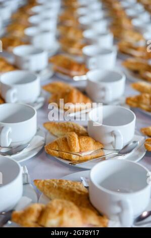 molte linee di croissant su un piatto con tazze da caffè vuote sul tavolo pronte per essere servite per una pausa tè durante una conferenza d'affari Foto Stock