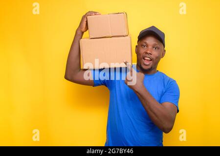 Un uomo di spedizione africano con cappuccio facciale, che punta alle scatole che sta portando sulla sua spalla Foto Stock