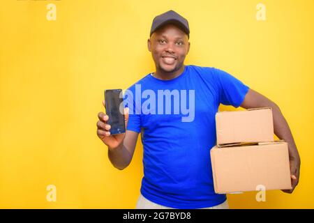 Un uomo di spedizione africano con cappuccio facciale, trasportando le scatole di consegna ed esponendo il suo smartphone Foto Stock