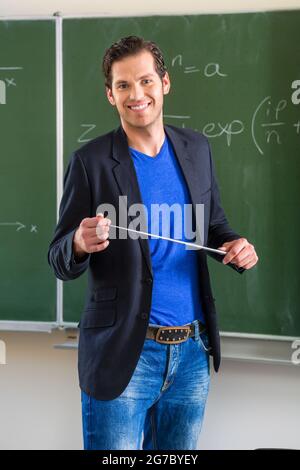 Insegnante o docente a scuola che tiene un puntatore davanti di una lavagna in classe scolastica Foto Stock