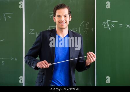 Insegnante o docente a scuola che tiene un puntatore davanti di una lavagna in classe scolastica Foto Stock