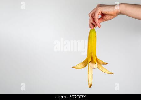 Banana sbucciata in una mano di donna su uno sfondo bianco. Foto Stock