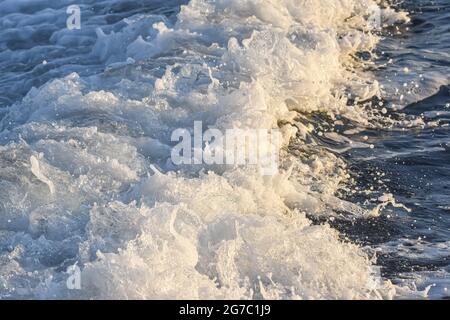 L'acqua di mare si è arenata a una schiuma sulla scia di una grande nave. Luce dorata nel tardo pomeriggio. Foto Stock