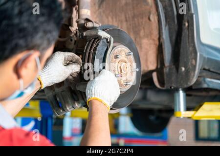 Le mani del meccanico dell'automobile sostituiscono i freni in garage. Tecnico meccanico addetto all'installazione della ruota dell'auto durante la manutenzione. Operatore che ha sostituito il disco del freno durante la riparazione automatica Foto Stock