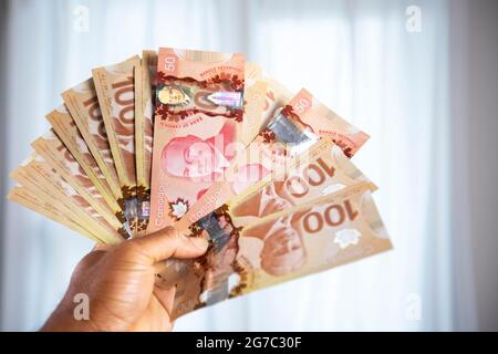 Mano dell'uomo che tiene le fatture canadesi di un centinaio di dollari e cinquanta dollari, soldi di carta. Foto Stock