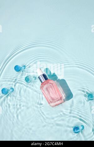 Mockup di bottiglia cosmetica rosa in vetro con pipetta e siero su superficie d'acqua con onde concetto di pubblicità detergente e idratante, invecchiamento nativo s. Foto Stock