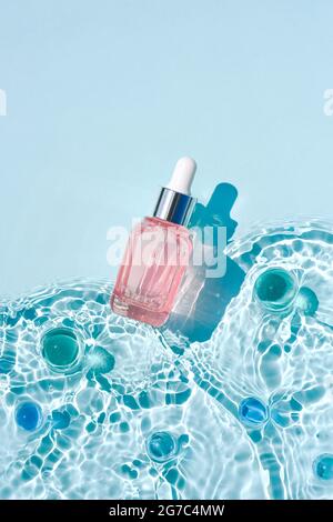 Mockup di bottiglia cosmetica rosa in vetro con pipetta e siero su superficie d'acqua con onde concetto di pubblicità detergente e idratante, invecchiamento nativo s. Foto Stock