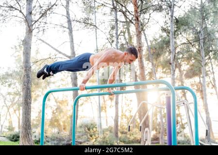 Vista laterale di un atleta maschile che si esercita su barre parallele. Foto Stock