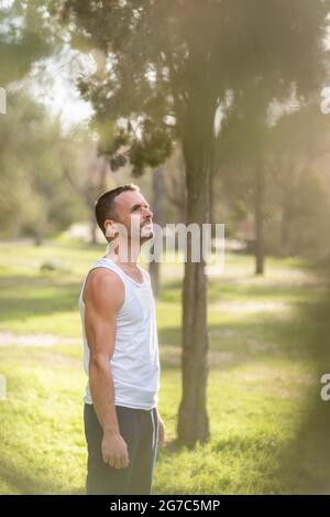 Uomo che indossa una t-shirt bianca senza maniche che si affaccia nel parco Foto Stock